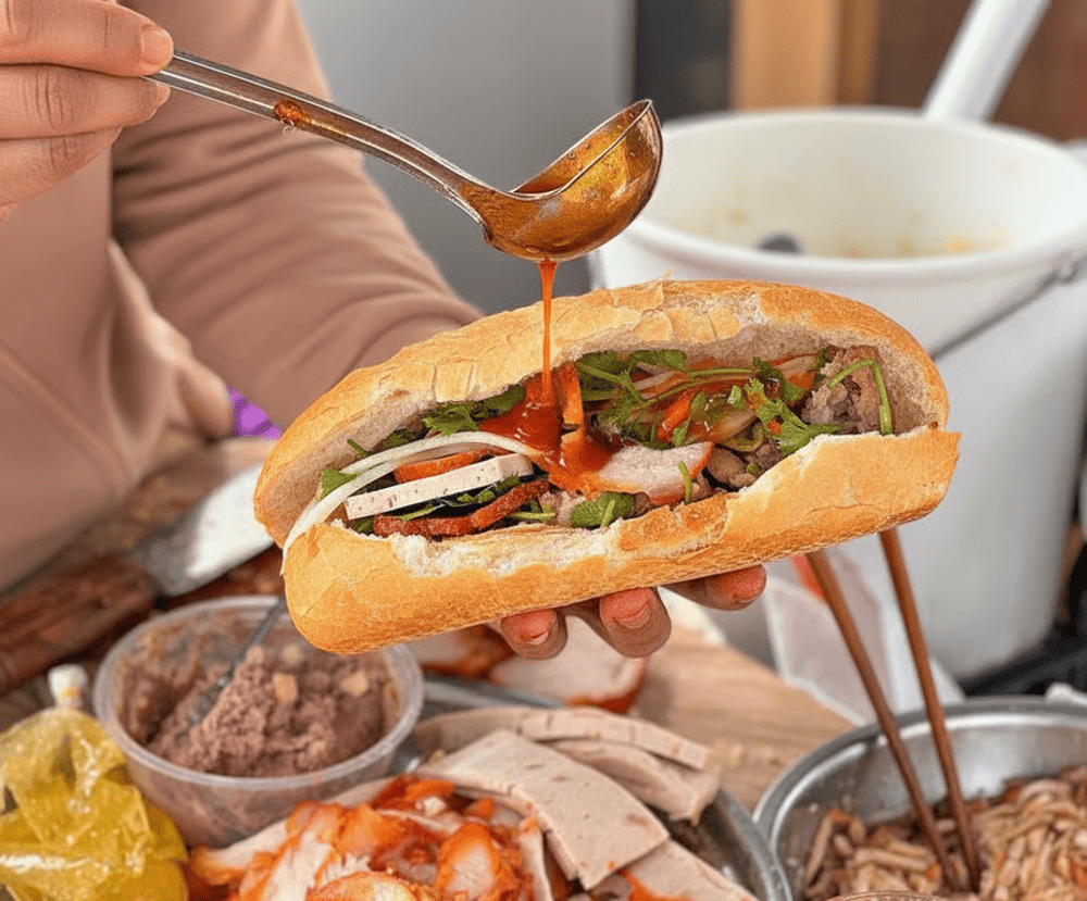 A crispy baguette (bạnh mi) filled with savory pork, pickled vegetables, and a rich sauce, perfect for a quick, flavorful meal